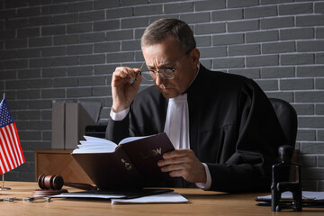 Mature judge reading law book at table in office