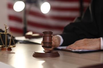 Mature judge with gavel at table in dark office, closeup