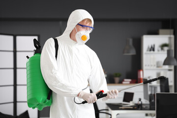 Male worker wearing hazmat suit with disinfectant cylinder in office
