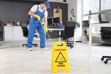 Male worker of cleaning service mopping floor in office