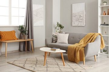 Interior of light living room with grey couch, table and shelf unit