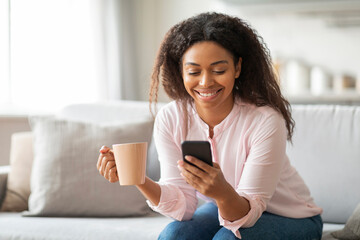 Lady holding coffee and smartphone on couch