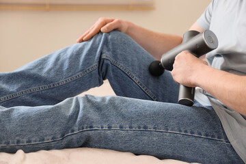 Young man massaging his leg with percussive massager in bedroom, closeup