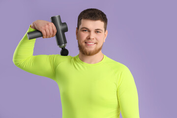Sporty young man massaging his shoulder with percussive massager on lilac background