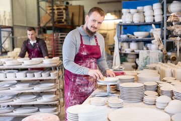 Positive skilled artisan carefully cleaning surface of freshly made plates with sponge, preparing...