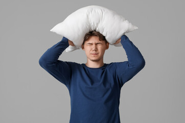 Young man with pillow suffering from headache on grey background