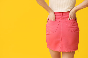 Legs of beautiful young woman wearing pink tight mini skirt on yellow background, back view