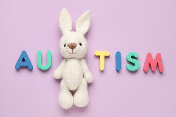 Word AUTISM, and toy bunny on lilac background. Top view