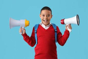 Happy little African-American schoolboy with megaphones on blue background