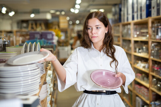Young woman looking for new plates at store of household goods