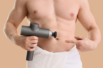 Naklejka premium Muscular young man pointing at percussive massager on beige background, closeup