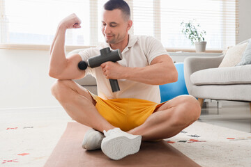 Sporty young man massaging his arm with percussive massager at home