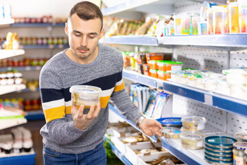 Adult male shopper in casual clothes chooses pickled herring in grocery store