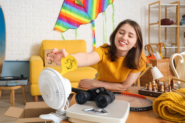 Young woman putting price on electric fan in room of unwanted stuff