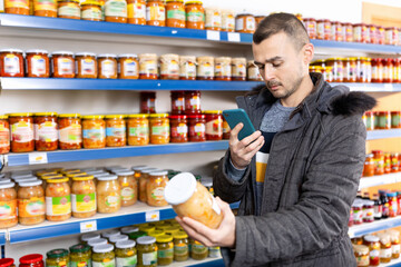 Man in store of imported Russian goods chooses jar with canned fermented cabbage. Male buyer...