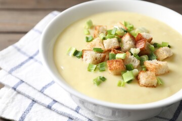 Tasty potato soup with croutons and green onion in bowl on table, closeup