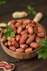 Fresh unpeeled peanuts and leaves in bowl on wooden table