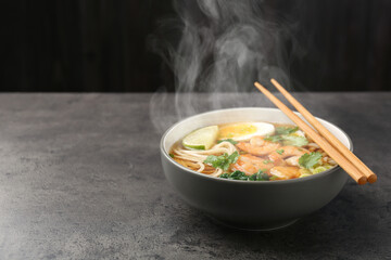 Delicious hot ramen with shrimps and chopsticks on grey table, space for text. Noodle soup