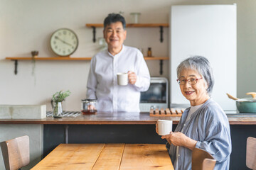 家のキッチンでコーヒーをいれる高齢者男性と高齢者女性（老夫婦）
