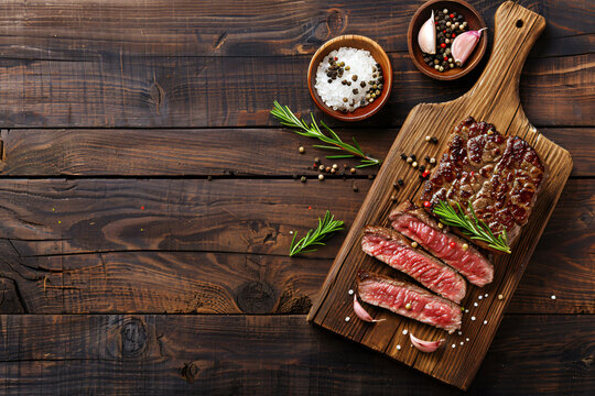 Raw organic marbled beef steaks with spices on a wooden cutting board on a black slate, stone or concrete background. Top view with copy space.