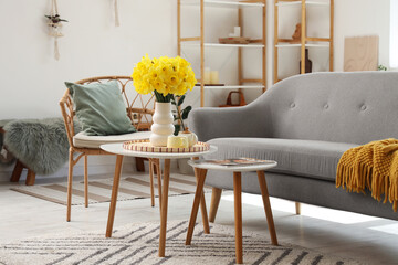 Interior of living room with grey sofa, carpet, coffee tables and vase of narcissus flowers