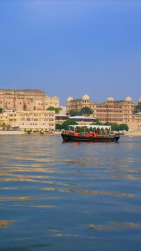 Famous tourist landmark Udaipur City Palace on the bank of lake Pichola with tourist boats - Rajput architecture of Mewar dynasty rulers of Rajasthan. Udaipur, India. Camera pan