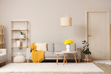 Comfortable sofa, shelving unit and coffee table with vase of narcissus flowers in living room - obrazy, fototapety, plakaty