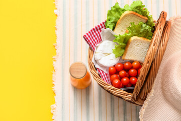 Wicker basket with tasty food and juice for picnic on yellow background. Top view