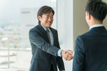 企業のオフィス・会議室で握手をして契約を結ぶビジネスマン
