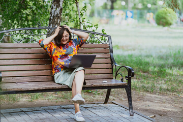 Asian businesswoman smiles conducting video meetings on her computer in nature. A cheerful woman engages in lively video calls on her laptop while sitting on a park bench surrounded by birch trees