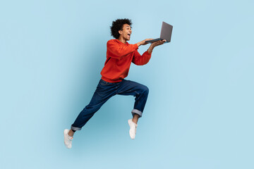 Playful man jumping with a laptop in hand