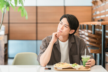 カフェでランチを食べながらグリーンスムージーを飲む若い男性（酵素・デトックス・食物繊維・健康食品）
