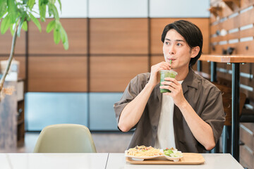カフェでランチを食べながらグリーンスムージーを飲む若い男性（酵素・ヘルシー・食物繊維・健康食品）
