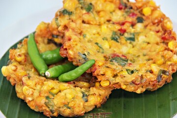 Bakwan Jagung or Dadar Jagung or Dadar Jagung Manado, is Manadonese style of corn fritters. Savoury snack made of corn, egg, flour, spring onion, pepper and salt. Served on a wooden plate.