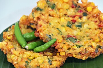 Bakwan Jagung or Dadar Jagung or Dadar Jagung Manado, is Manadonese style of corn fritters. Savoury snack made of corn, egg, flour, spring onion, pepper and salt. Served on a wooden plate.