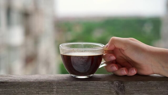 Person holds transparent cup filled with aromatic espresso. Relaxed woman holds hot mug and takes moment to enjoy freshly brewed espresso