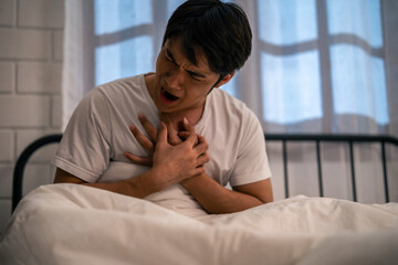 Asian young man feeling heart attack while sleeping on bed at night. 