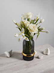 White flowers in a translucent ribbed vase, stones lie against a white wall