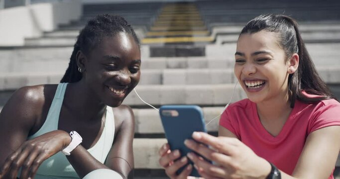 Happy woman, friends and fitness with phone listening to music, audio streaming or relax on break at stadium. Female person or athletes smile in rest on bleachers with mobile smartphone for podcast