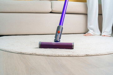 Woman cleaning Carpet with cordless Vacuum cleaner. Housewife using wireless Vacuum for big...