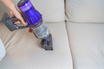 Woman cleaning Sofa with cordless Vacuum cleaner. Housewife using wireless Vacuum for big cleaning home. Housework, Housecleaning, Housekeeping, Removes dust, Domestic hygiene and daily routine