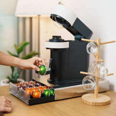 hand making Espresso Coffee by Coffee Maker Machine with Capsule of roasted coffee bean on wood table bar. Daily beverage drink at Home, Apartment and Office concept