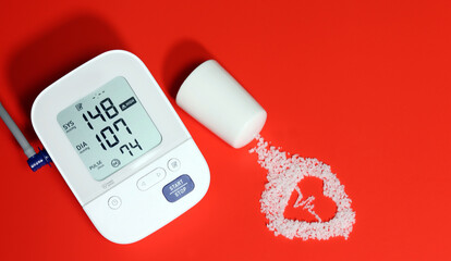 Electronic blood pressure gauge and electrocardiogram-shaped salt on a red background. Eating salt...