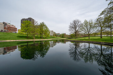 Buildings of Saint Louis, Missouri reflected in reflecting pool in Gateway Arch National Park on overcast April morning. - obrazy, fototapety, plakaty