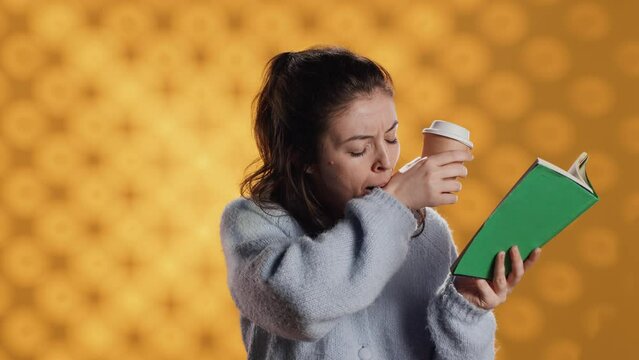 Tired woman reading book, holding cup of coffee, isolated over studio background. Exhausted bookworm enjoying novel and caffeine beverage, lacking energy, struggling to stay awake, camera A