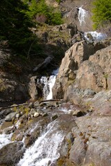 Water cascading and splashing down and around rocky cliff face, partially in shadow. 