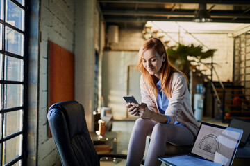 Woman using smartphone with laptop on desk in modern industrial office