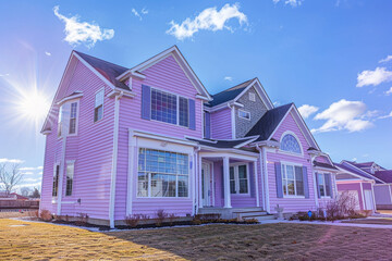 A pastel lavender house with siding, on a large lot in a suburban setting, boasting traditional...