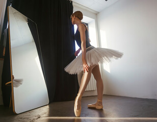 young ballerina in a tutu and pointe shoes standing in front of a mirror poses ballet elements...