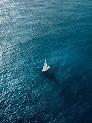 A sailboat is floating in the ocean. The water is calm and blue. The boat is the only object in the image